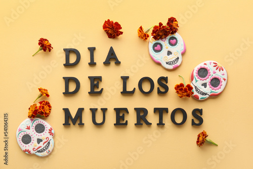 Text DIA DE LOS MUERTOS with skull shaped cookies and flowers on yellow background © Pixel-Shot