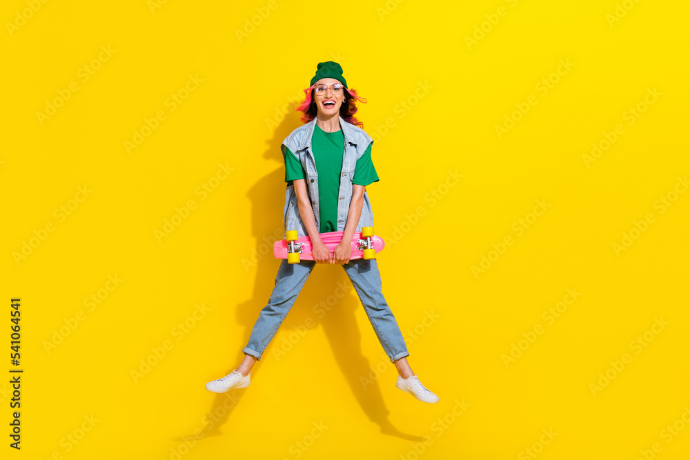 Portrait of flying cheerful optimistic girl curly hairdo wear green t-shirt hold skateboard flying isolated on yellow color background
