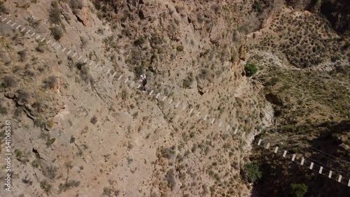 Man overcomes his fears by crossing a suspension bridge that crosses a valley. via ferrata Bird's eye view rotating on the climber.