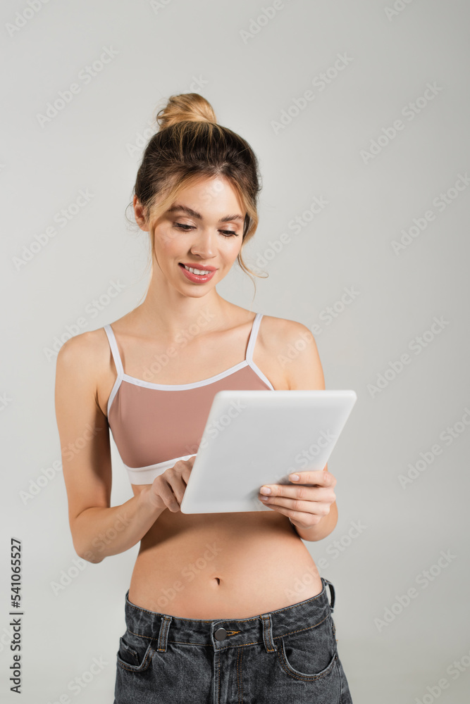 smiling woman with perfect skin and slender body using digital tablet isolated on grey smiling woman with perfect skin and slender body using digital tablet isolated on grey