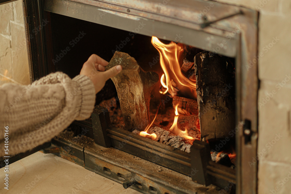 Heating house in winter with wood burning stove. Woman throwing
