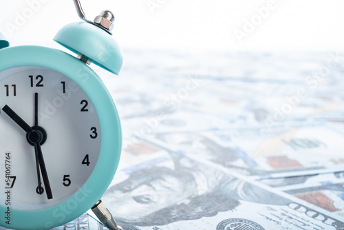 A small alarm clock stands on dollar bills.