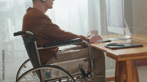 Caucasian wheelchaired businessman in headphones working on computer at home office photo