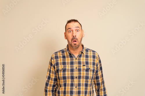 Handsome man wearing plaid shirt standing over isolated beige background scared and shocked with surprise expression, fear and excited face