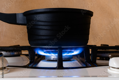 Black metal pot on gas stove close-up on blurred kitchen background. Side view