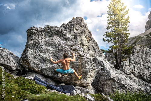 Sporty shirtless man climbs on boulder problem in the afternoon. Falzarego pass, Dolomites, South Tirol, Italy, Europe.