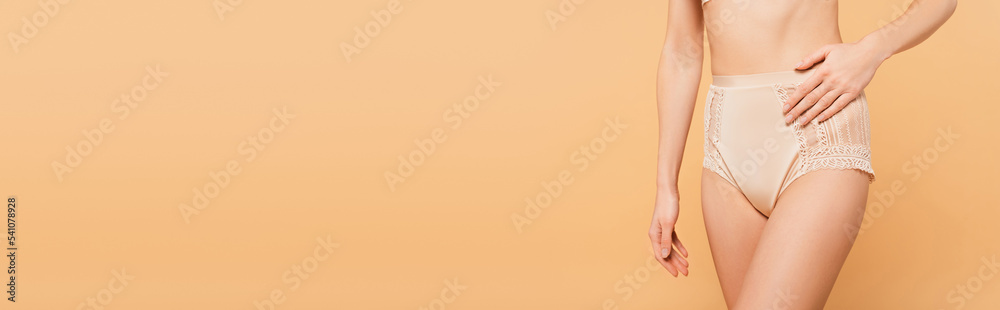 cropped view of fit woman touching lace panties isolated on beige, banner cropped view of fit woman touching lace panties isolated on beige, banner