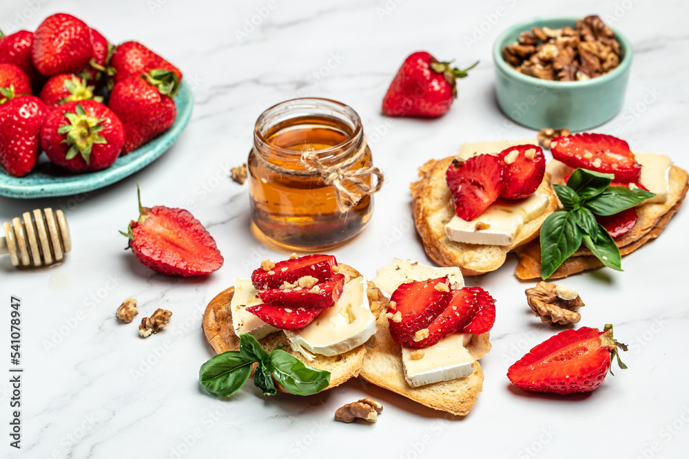Two toasts or bruschetta with trawberries, cheese camembert nuts and honey. Summer breakfast. Healthy, clean eating. Vegan or gluten free diet Two toasts or bruschetta with trawberries, cheese camembert nuts and honey. Summer breakfast. Healthy, clean eating. Vegan or gluten free diet