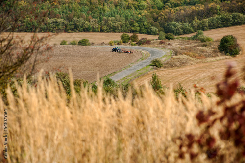 autumn landscape with dry grass, road across agricultural fields, tractor wor...