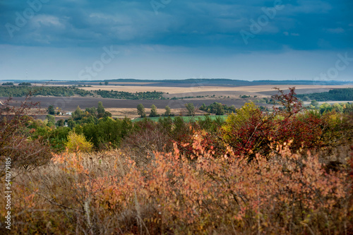 landscape of farmland with village in autumn with colorful trees and dramatic...