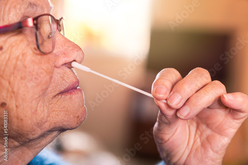 Portrait of old woman taking a self swabbing home tests Covid19 with antigen kit
