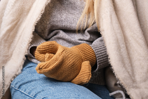Frozen. A young woman sits on the floor in an apartment in a warm sweater, plaid and mittens and is shivering from the cold. Problems with the heating system in the cold season of the year