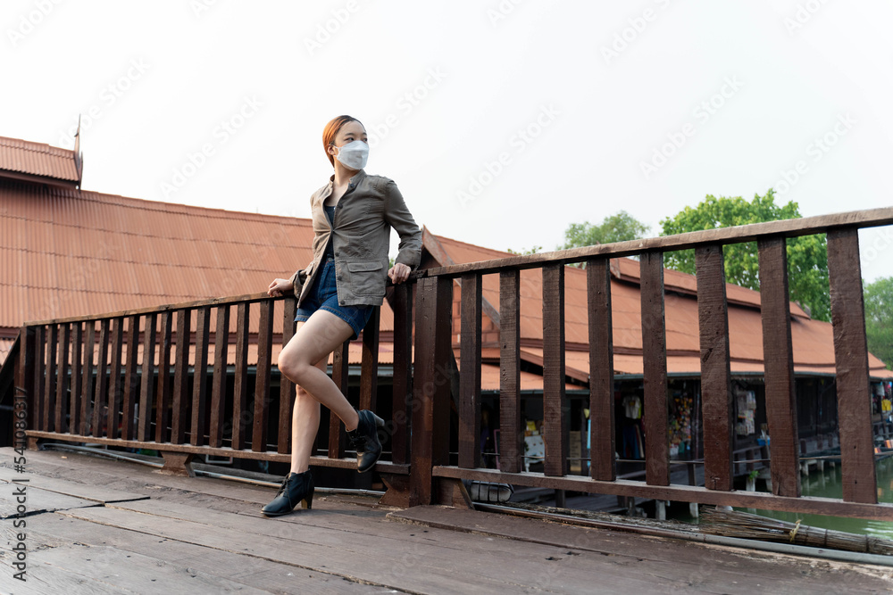 Young asian woman traveler with mask and backpack posting on the bridge in the morning