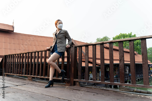 Young asian woman traveler with mask and backpack posting on the bridge in the morning