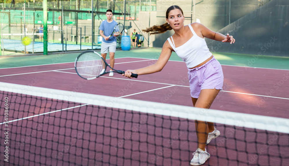 Young woman in shorts playing tennis on court. Racket sport training outdoors.