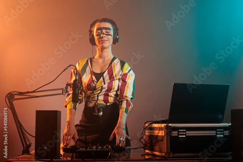 Happy female performer working as dj with turntables, mixing techno music with bass and audio equipment. DJ woman playing songs at mixer, standing over colorful background with smoke. photo