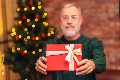 an elderly man in a green knitted with gift box near the Christmas tree