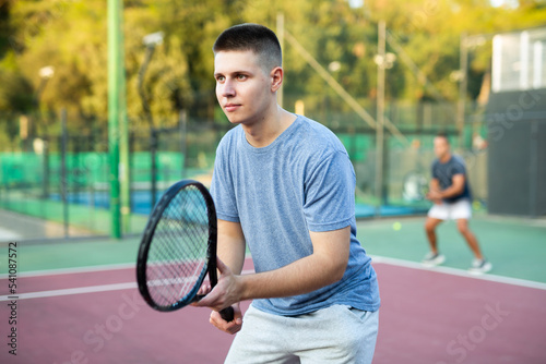 Young teenage tennis player training on court. Boy using racket to hit ball. © JackF