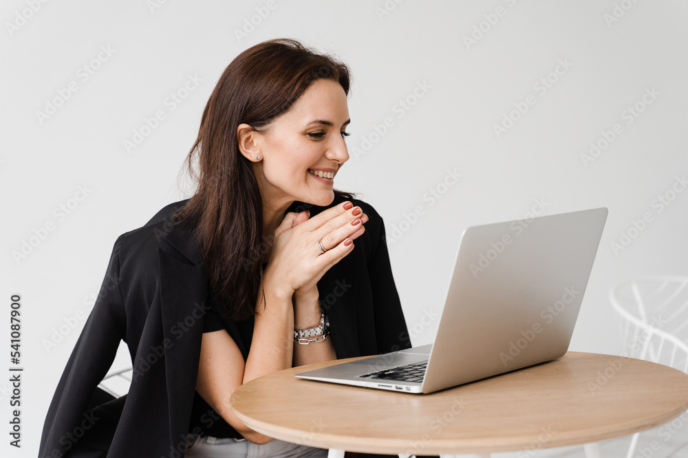 Happy girl chatting with family and friends via video call on white background. Successful business woman with laptop works remotely and laughs with colleagues in online video meeting. Happy girl chatting with family and friends via video call on white background. Successful business woman with laptop works remotely and laughs with colleagues in online video meeting.