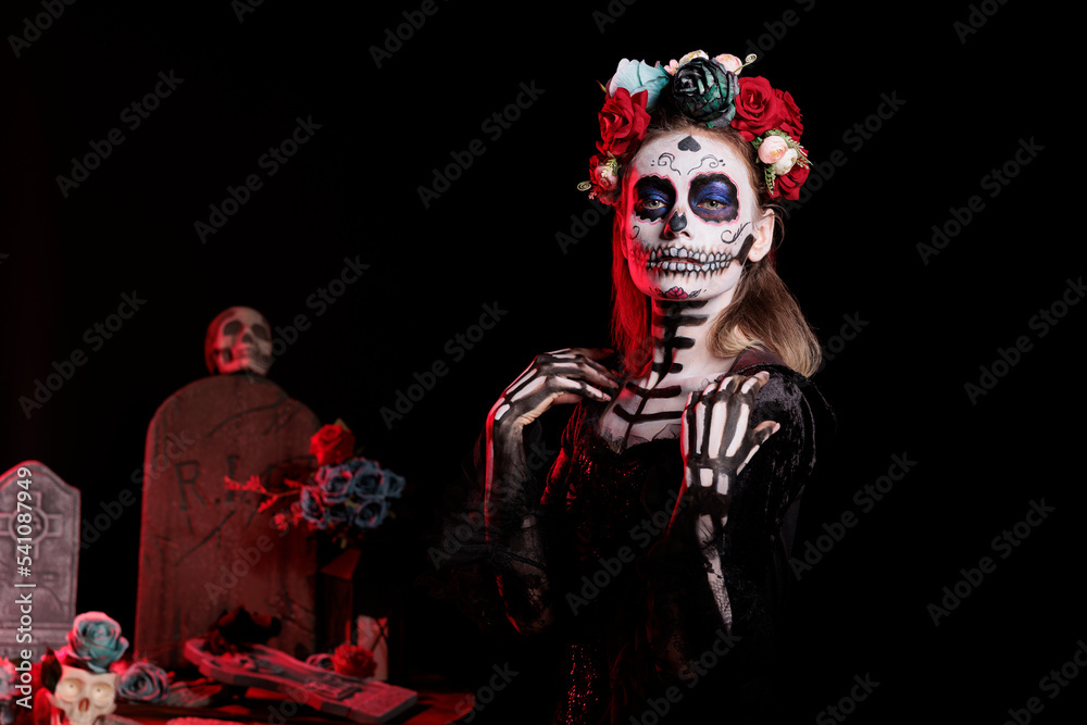 Young creepy adult wearing traditional body art on halloween day of the dead, having flowers crown. Female model with black and white make up and holy santa muerte costume on holiday. Young creepy adult wearing traditional body art on halloween day of the dead, having flowers crown. Female model with black and white make up and holy santa muerte costume on holiday.