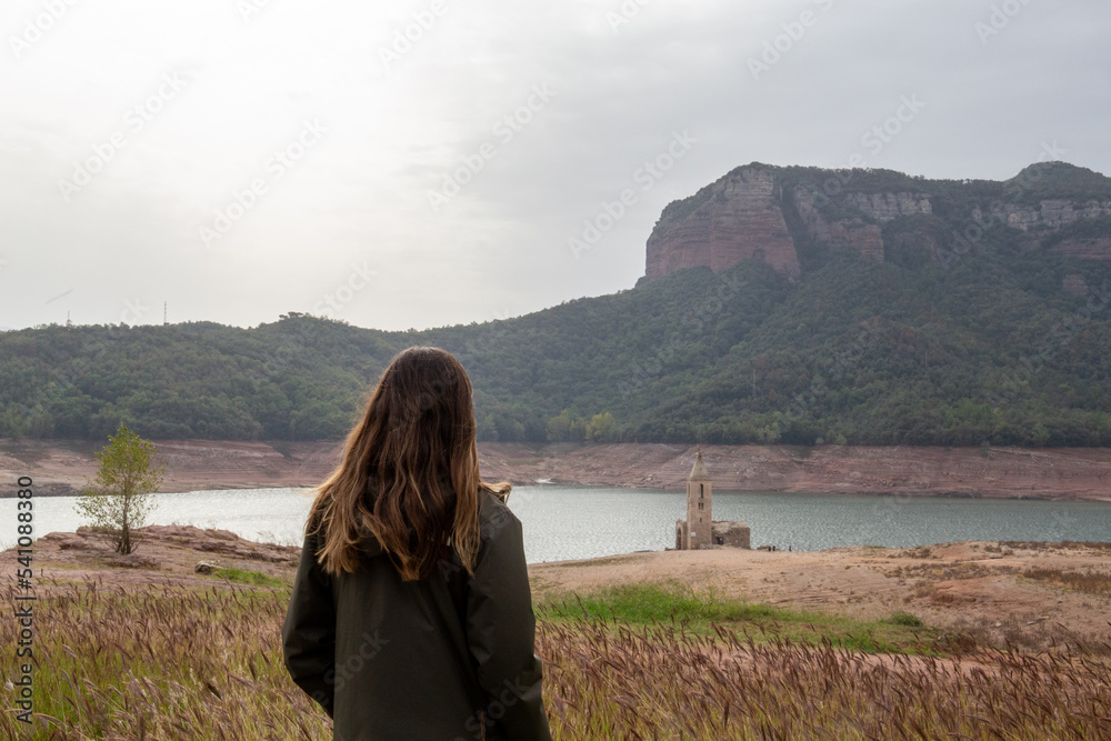 woman from the back looking at a reservoir with little water due to the drought and the little rain effect of global warming