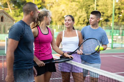 Group of young men and women having conversation about tennis game on outdoor court.