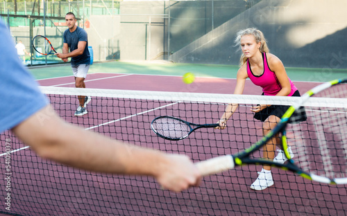 Young woman playing tennis against man on court. Racket sport training outdoors.