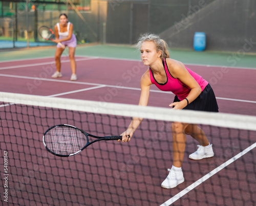 Portrait of concentrated energetic girl playing tennis outdoors, preparing to hit forehand to return ball close to net