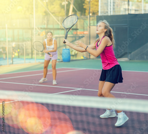 Positive attractive female player hits ball close to net while playing tennis in rays of sun and glare. Female fitness concept © JackF
