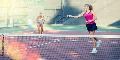 Young woman in skirt playing tennis on court. Racket sport training outdoors.