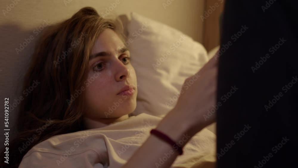 Pretty tired young woman straightens her curly hair while lying in bed and continues to read message on phone. girl watches movie or chats with her friends late at night on smartphone. Pretty tired young woman straightens her curly hair while lying in bed and continues to read message on phone. girl watches movie or chats with her friends late at night on smartphone.