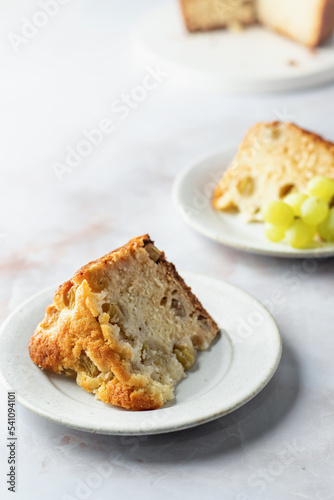 Slice of homemade biscuit cake or pie with white fresh grapes on a white marble background with text space