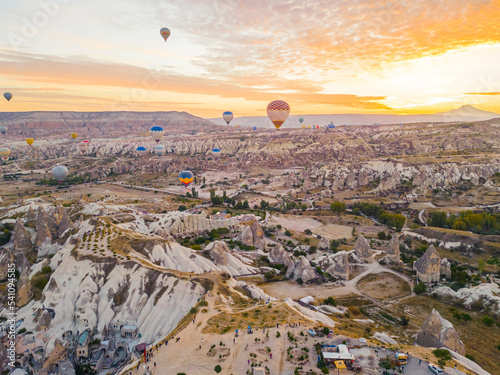 Mountainous landscape of Cappadocia, Turkey with colorful hot air balloons flying in the air in the evening with bright orange sunlight. Horizontal shot. High quality photo