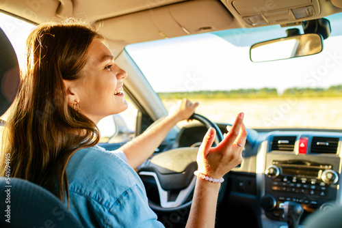 pretty woman singing while driving a car on road trip on summer day