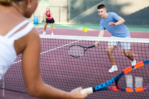 Young man in shorts and t-shirt playing tennis against woman on court. Racket sport training outdoors.