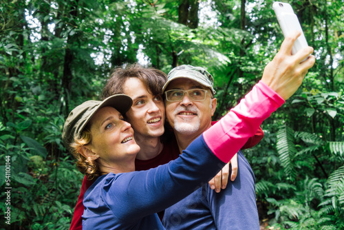 Parents and child taking a selfie while hiking in a tropical forest.