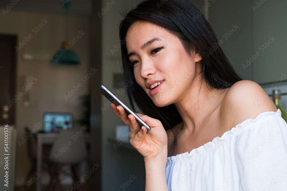 Young chinese girl sending a voice message with her smartphone inside her house Young chinese girl sending a voice message with her smartphone inside her house