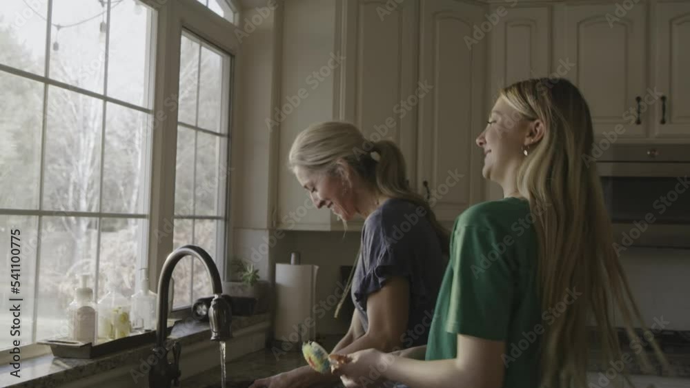 Smiling mother and daughter washing dishes and singing to music / Highland, Utah, United States