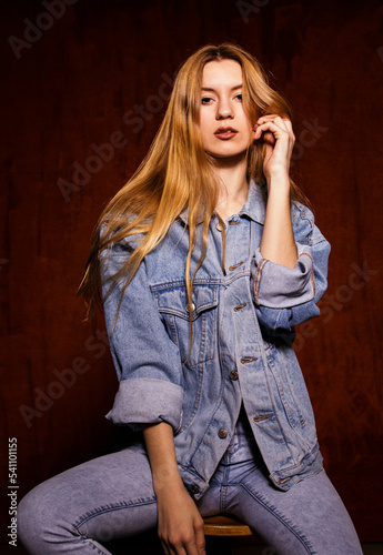 Young adult woman sitting on a chair in a studio looking at camera wearing all denim looking at camera.