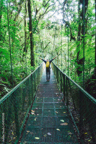 Unrecognizable person walking down a bridge in the middle of a tropical forest spreading his hands wide open.