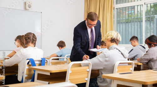 Group of focused teenage students sitting at classroom working at class with helpful teacher