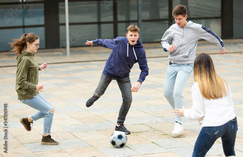 Teen friends spending time together outdoors playing with ball on square near school