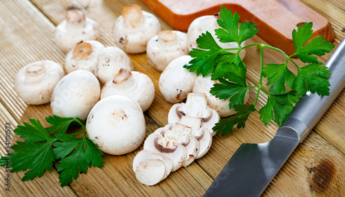 Close-up of cut fresh champignons with greens on wooden desk in kitchen