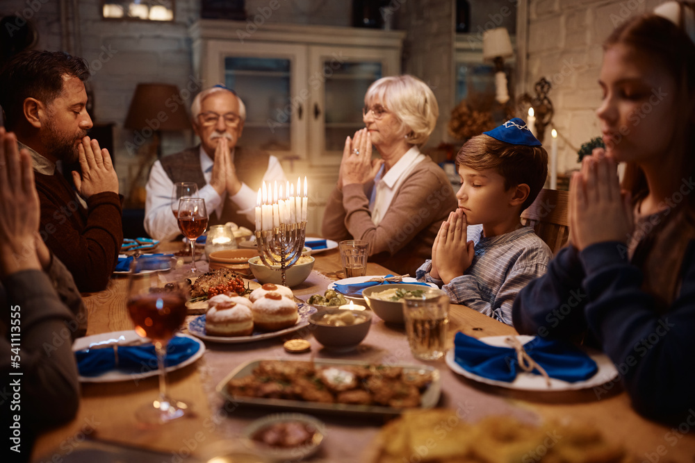 Multigeneration Jewish family praying at dining table on Hanukkah.