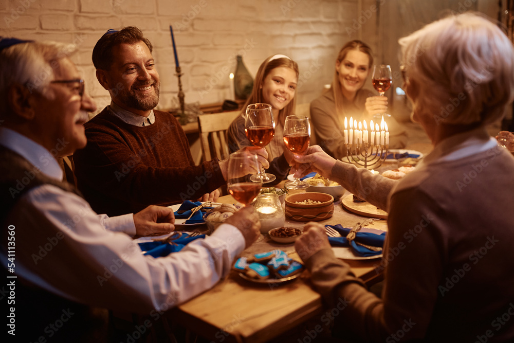 Happy man toasting with his family during dinner at dining table on Hanukkah.