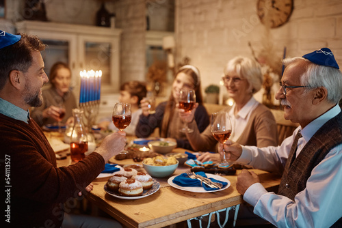 Happy multigeneration Jewish family toasting during meal at dining table on Hanukkah.