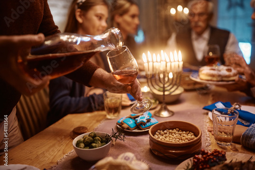 Close up of Jewish man pouring wine into wineglass while celebrating Hanukkah with his family at dining table.