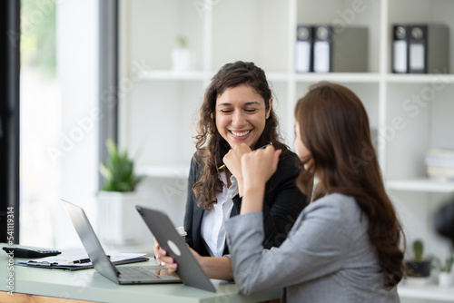 Cheerful young female entrepreneur browsing tablet and laptop at workplace in office.
