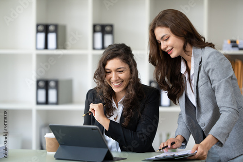 Cheerful young female entrepreneur browsing tablet and laptop at workplace in office.