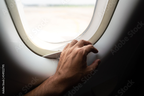 Hand of a passenger places on airplane's window, ready to departure. Safe flight transportation and journey abstract photo. Photo contained high contrast ration and black shadow area.